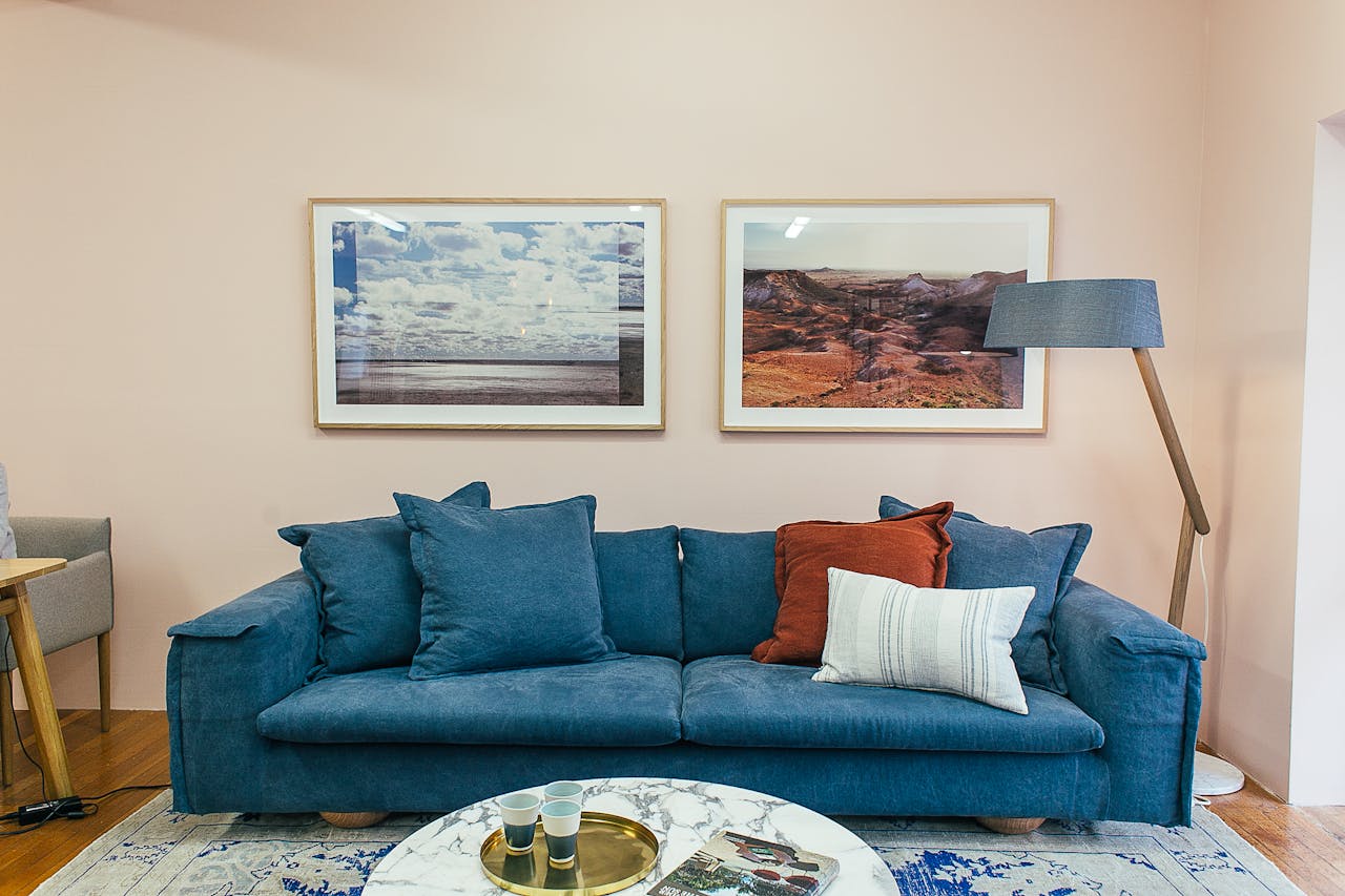 services-04 Big comfortable blue sofa with soft cushions placed in modern living room with round marble table near wall decorated with framed pictures